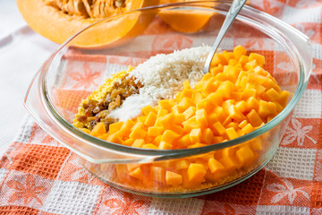 Raw washed millet, rice, raisins and pumpkin in a glass pan in the process of preparing milk pumpkin porridge