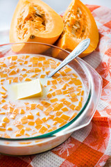 Raw pumpkin, milk and butter in glass pan in the process of preparing pumpkin porridge with raising