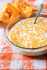 Raw pumpkin and milk in glass pan in the process of preparing pumpkin porridge with raising