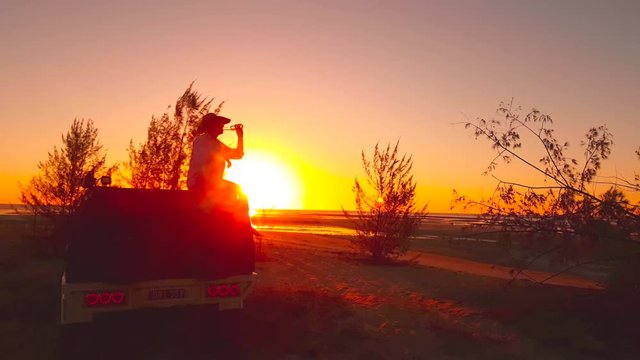 cowboy, ringer from the outback in the north end of Australia having a beer on the roof of his ute at the beach in the sunset.