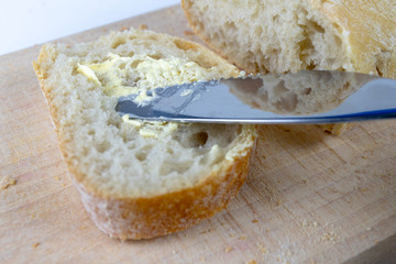 Fresh bread on a wooden kitchen board. A slice of bread smeared with butter.
