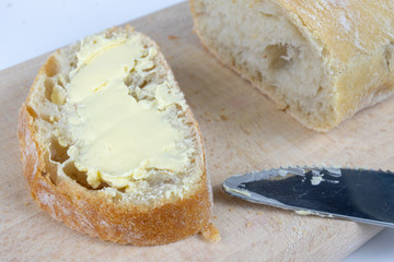 Fresh bread on a wooden kitchen board. A slice of bread smeared with butter.