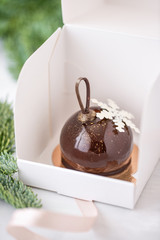 Mini mousse pastry dessert with chocolate glazed Individually wrapped in white box. The branches of spruce on bokeh background. Modern european cake. French cuisine. Christmas . Snowflake