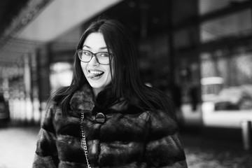 girl with beautiful makeup in fur coat shows tongue and grimace on black and white photo