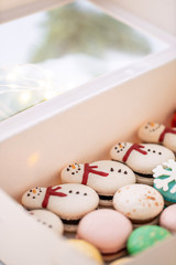 Variety of sweet macaroons in white box. The branches of spruce on bokeh background. Modern european French cuisine. Christmas theme, Merry Christmas card. New year mood. lights of garland bulbs