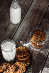 Glass with fresh milk and homemade chocolate chips cookies over a wooden table. 