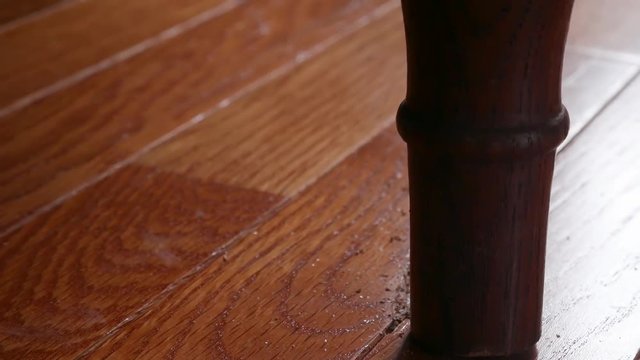 Close up shot of a bedpost scratching a hardwood floor as the bed is being shaken suggestively from activity above.