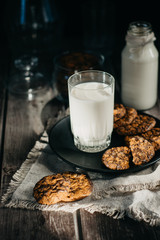 Glass with fresh milk and homemade chocolate chips cookies over a wooden table. 