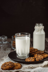 Glass with fresh milk and homemade chocolate chips cookies over a wooden table. 