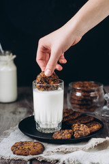 Glass with fresh milk and homemade chocolate chips cookies over a  on wooden table. Breakfast .Dipping chocolate cookie in glass of milk