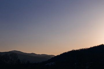evening sky and silhouettes of mountain peaks and several buildings on the slopes of the mountain