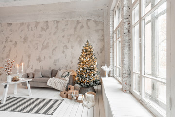 Light living room with Christmas tree. Comfortable sofa, high large Windows. Light white brick wall.