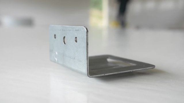 Close up shot of a metal bracket on a table as a contractor walks by in the background