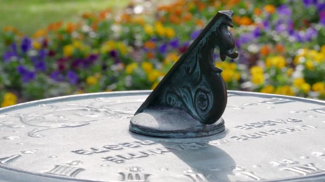 Athens, GA - October 9, 2018: Slow pan of a tight shot on a sundial in a relaxing garden with flowers in bloom on a beautiful and sunny spring morning.