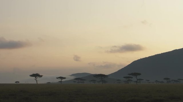 Sun rising behind the sloping mountains and tree lined landscape in Mara Maasai national park