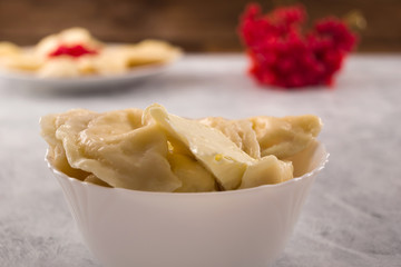 Dumplings with filling and butter in white bowl, wooden background.