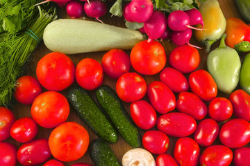 Fresh vegetables tomatoes, cucumbers, zucchini, peppers, greens, radishes and mushrooms on the kitchen table.