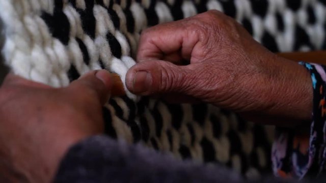 Close up in hands of a lady weaving a natural wool horse riding blanket. Trapa Trapa Alto Biobio. Chile. Flat plane