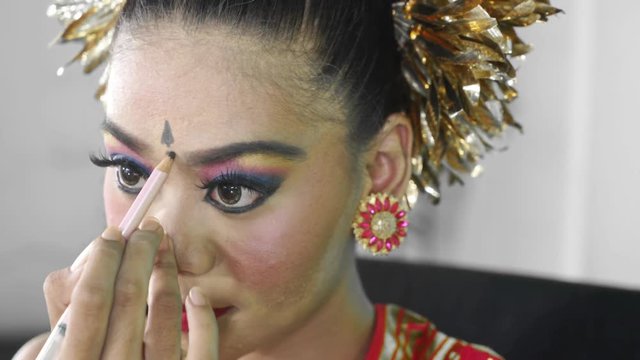 Closeup of female traditional Pendet dancer applying makeup on her face. Pendet Dance is a traditional dance from Bali, Indonesia. Shot in 4k resolution