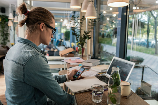 Digital age. Smart young man sitting in front of the laptop while holding a smartphone in his hands