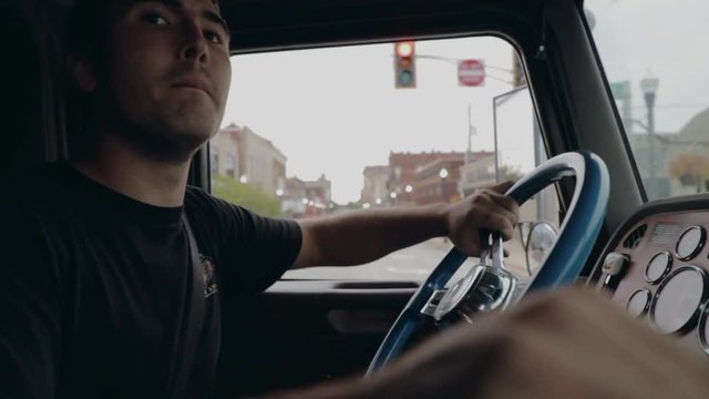 Young truck driver shifting gears driving through city in cockpit view