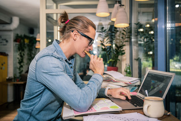 Tasty snack. Smart young man eating a tasty sandwich while looking at the laptop screen