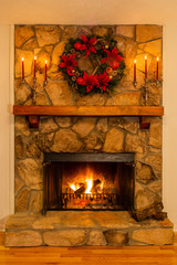 Stone fireplace with a glowing fire decorated with a wreath and candelabras.