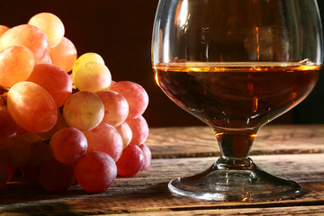 Cognac or Brandy in a glass and fresh grapes, still life in rustic style, vintage wooden background, selective focus.