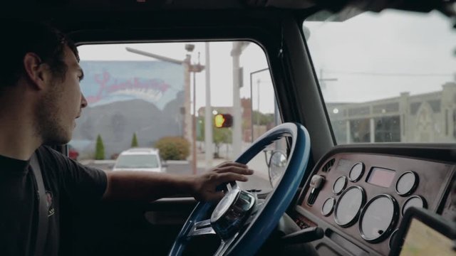 Young truck driver shifting gears driving through city in cockpit view in slow motion