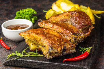 Barbecued pork ribs seasoned with a spicy bbq sauce served with fries on an old rustic wooden chopping board in a country kitchen