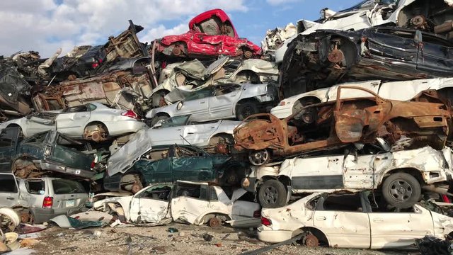 Cars in scrap yard stacked up in sunlight with varying colors and conditions; pan from left to right.