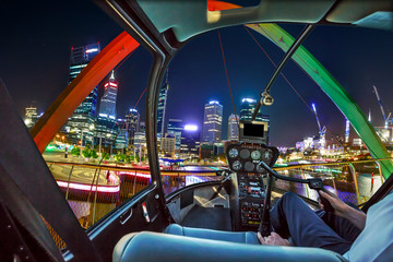 Helicopter cockpit interior flying on Elizabeth Quay Bridge by night on Swan River at entrance of Elizabeth Quay marina. Scenic flight above Perth, Western Australia skyline. Night urban aerial scene.