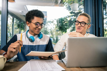 University education. Joyful positive man holding his notebook while preparing university home task