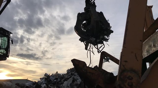 Slow motion claw on crane in junk yard hovers over crushing machine before dropping metal for recycling purposes. 