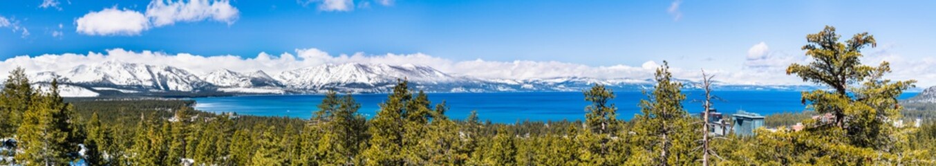 Panoramic view towards Lake Tahoe on a sunny clear day; the snow covered Sierra mountains in the background; evergreen forests in the foreground