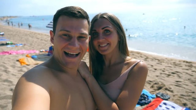Young happy couple taking self portrait on sea beach. Smiling pair doing selfie at the ocean shore. Cheerful man and woman enjoying honeymoon vacations and having fun at seaside. Concept of resting