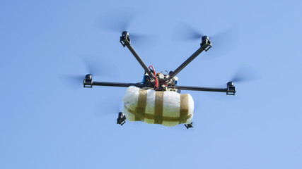 CLOSE UP: Illegal cargo drone flying big narco drugs package against blue sky - obrazy, fototapety, plakaty