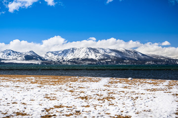 South Lake Tahoe snow covered sandy beach, on a sunny day; the snow covered Sierra mountains in the background; California