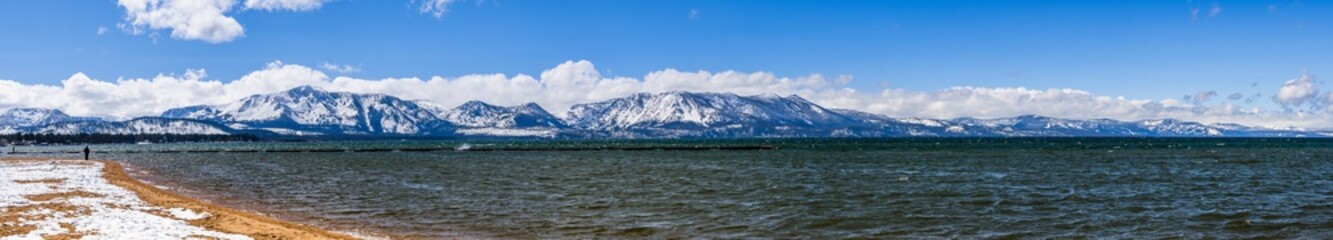 South Lake Tahoe shoreline and snow covered sandy beach, on a sunny day; the snow covered Sierra mountains in the background; California