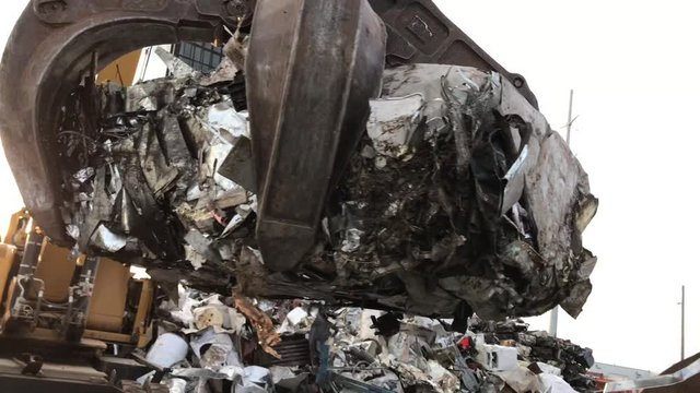 Junk yard claw close up clamping crushed metal in air and setting down onto flatbed semi truck for recycling trip thereafter. 