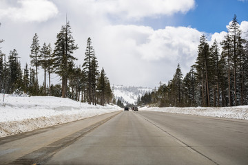 Cars driving on I80 interstate through the Sierra mountains close to lake Tahoe on a sunny winter day; the road has been cleared on snow, California