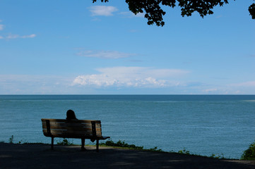 Solitary silhouette relaxing on bench by great lake