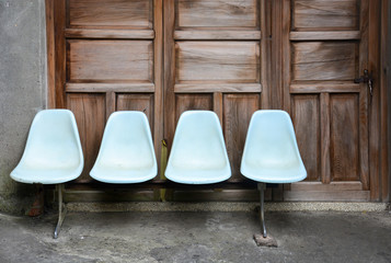 bench, row of old light blue plastic chairs on cement floor with wooden door background, lonely...