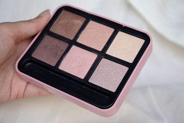 Woman holding palette of cosmetic eye shadow, pink shades.