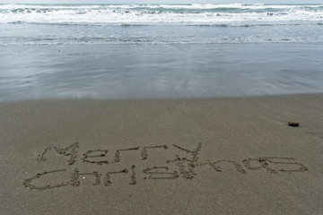 Fototapeta premium Merry Christmas written in the sand with wet sand behind