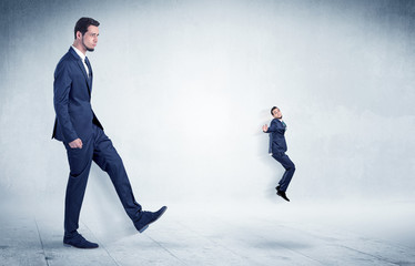 Big businessman kicking small businessman who is flying away with his briefcase on his hand
