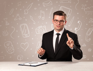 Young handsome businessman sitting at a desk with white mixed media icons behind him