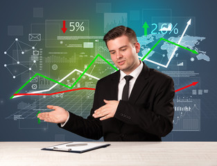 Young handsome businessman sitting at a desk with stocks and progress charts behind him