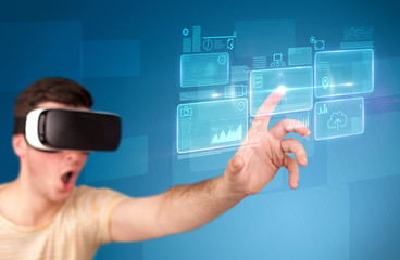 Young impressed man wearing virtual reality goggles with blue squares containing data at his fingers 