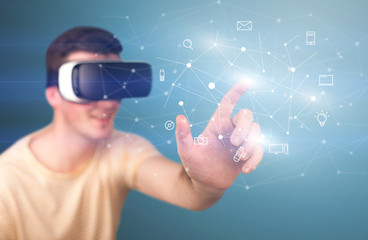 Young impressed man wearing virtual reality goggles with mixed media icons around his finger